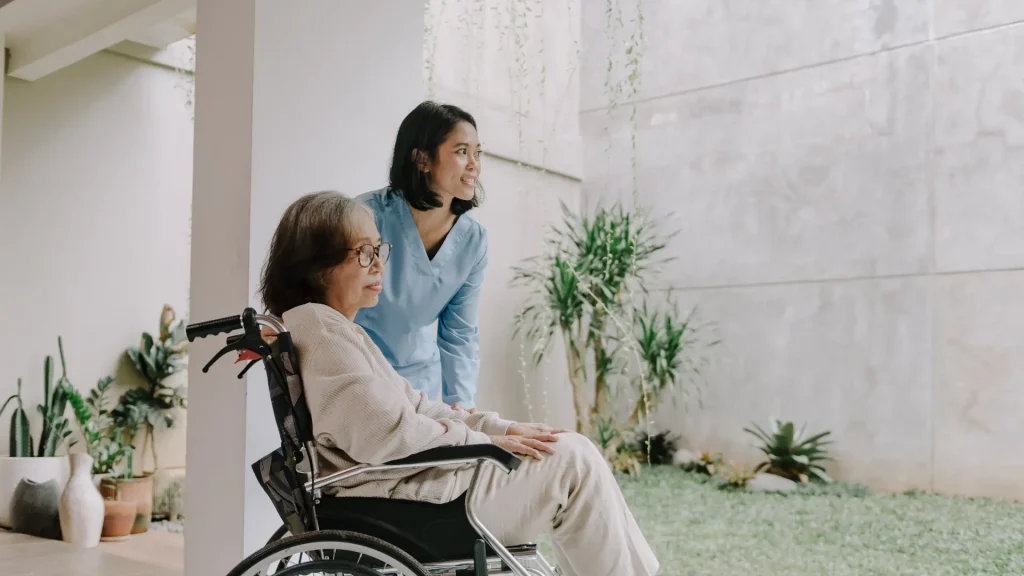 A caregiver assisting an elderly woman in a wheelchair while looking outside.