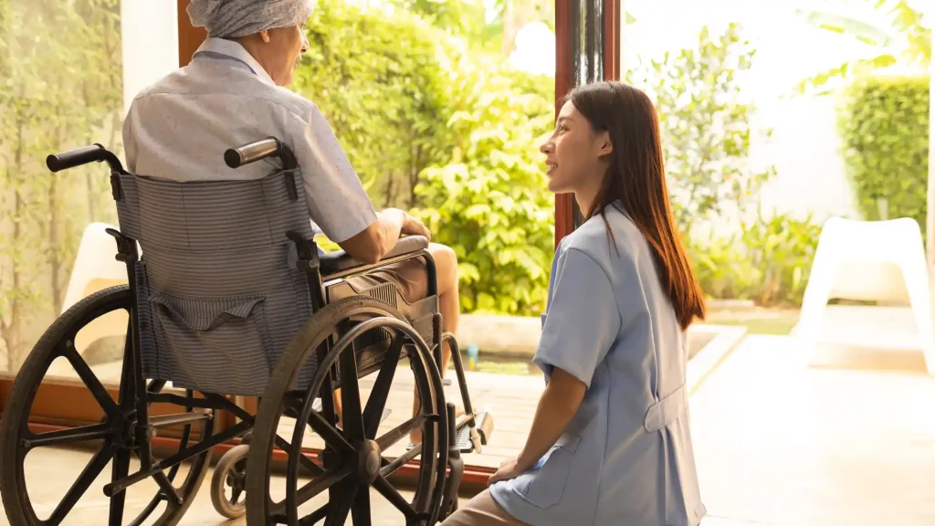 A caregiver talking to an elderly person sitting in a wheelchair, with a bright and peaceful outdoor background